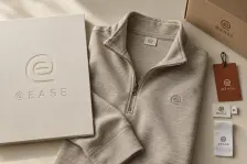 The fictional athleisure identity At Ease shown as an embossed brand board, quarter-zip garment, woven and care labels, swing tag and delivery carton.