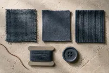 One indigo rendered on five substrates in a row, a coarse woven, a jersey, a rib, a wound thread card and a button, each landing a shade away from the one beside it
