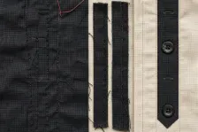 A dark panel covered in unpicked stitch lines, holes and loose thread ends with two removed strips lying beside it, next to a resolved cream and dark placket